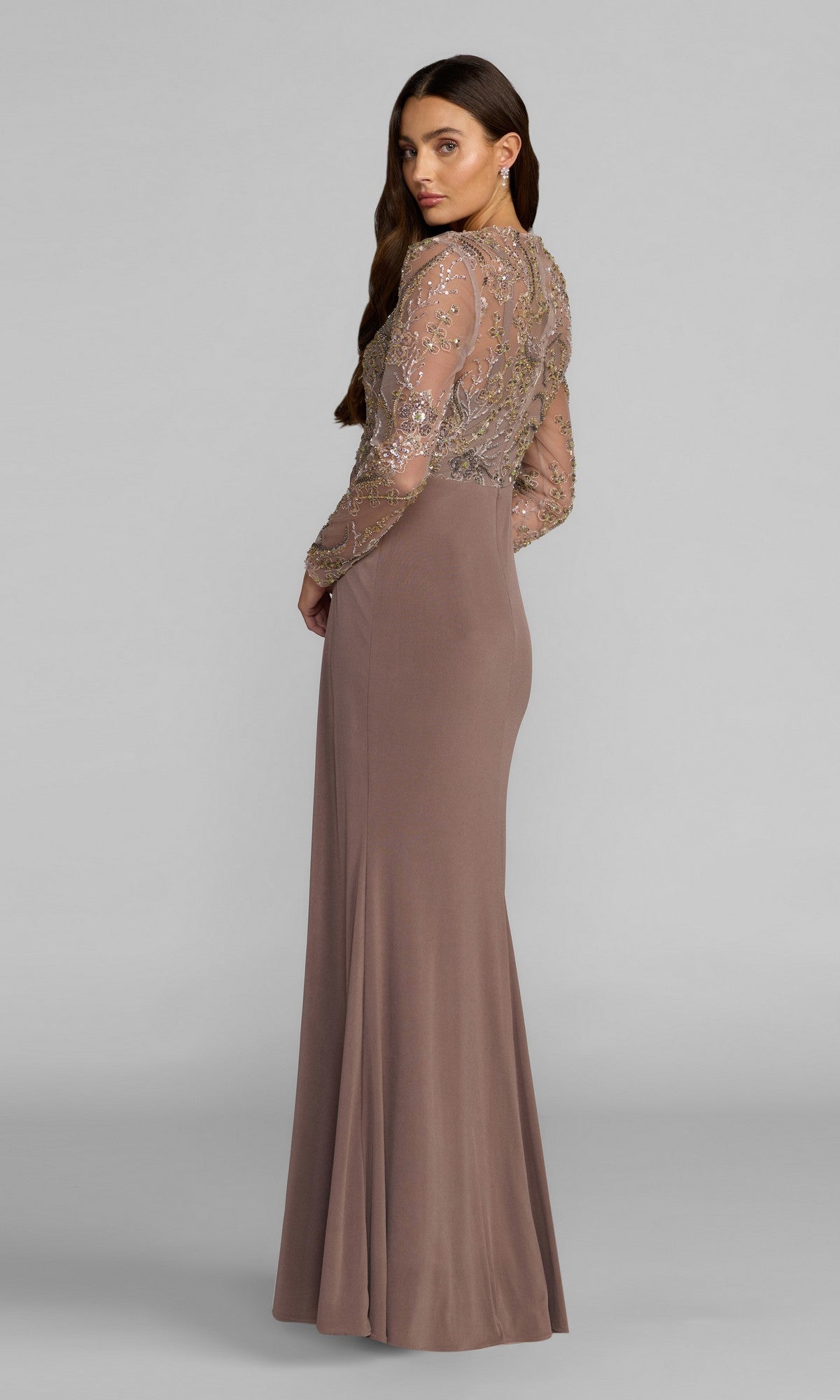 A woman wearing the Mac Duggal 69121 long formal dress in mauve, featuring a floor-length silhouette, sheer embellished long sleeves, a back panel, and a sequin-embroidered bodice, stands facing away from the camera.